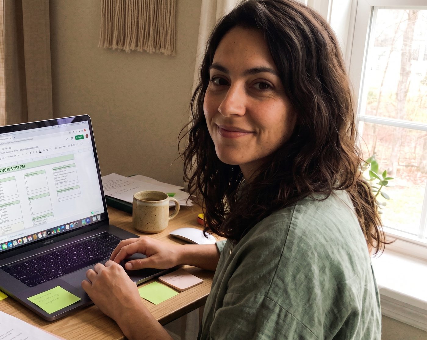 Layla at her desk, working on an ADHD planner in Google Sheets, cup of tea and sticky notes nearby